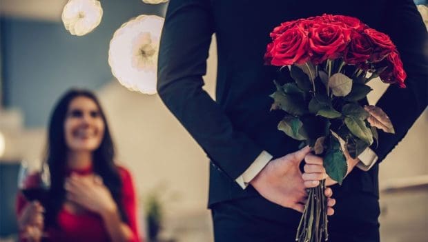 man hiding roses behind his back, woman is excited