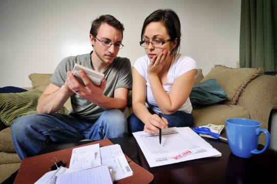 Young couple sitting on couch reviewing over due credit card statements.