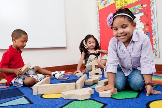 Three young children playing with building blocks in a public elementary school.