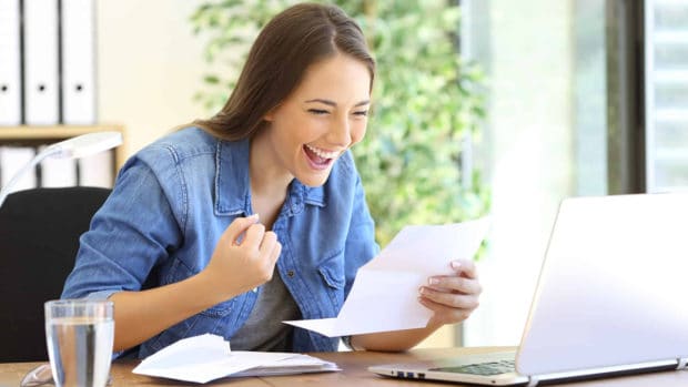 Excited entrepreneur woman reading good news in a letter in a desktop at office
