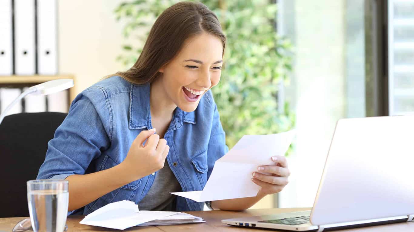 Excited entrepreneur woman reading good news in a letter in a desktop at office