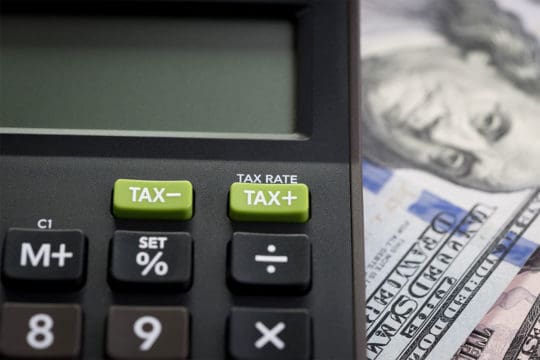 How Long Should I Keep Receipts For Tax Purposes? TAX RATE on calculator with background of blurred US Dollar banknotes.