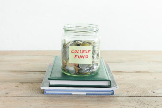 Coins in glass jar with College Fund label and books. Money savings, education or college fund, planning concept, copy space.