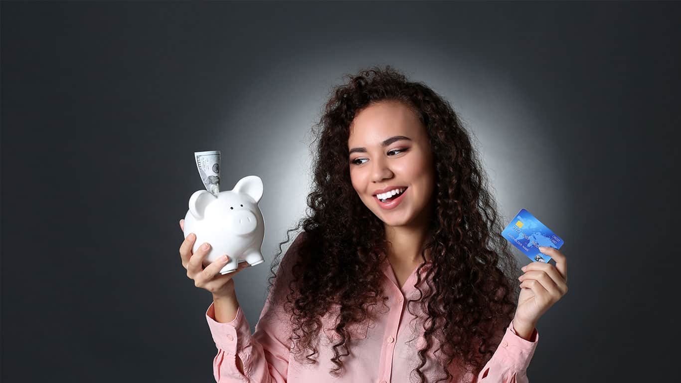 Beautiful young girl holding piggy bank and credit card on grey background