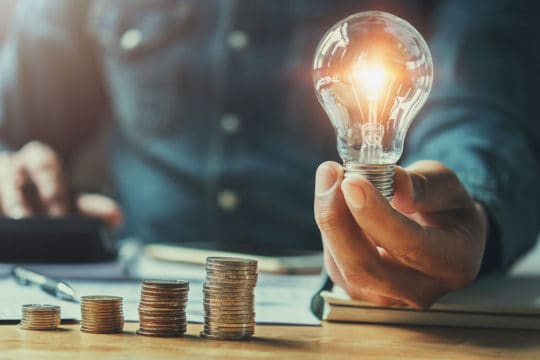 Business man hand holding lightbulb with using calculator to calculate and money stack