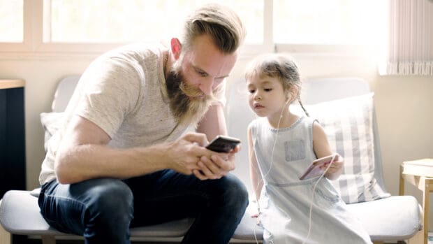 Single father looking at his phone while his daughter looks on