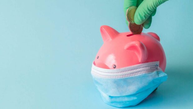 Piggy bank with protective facemask and hand in glove putting euro coins on isolated background.