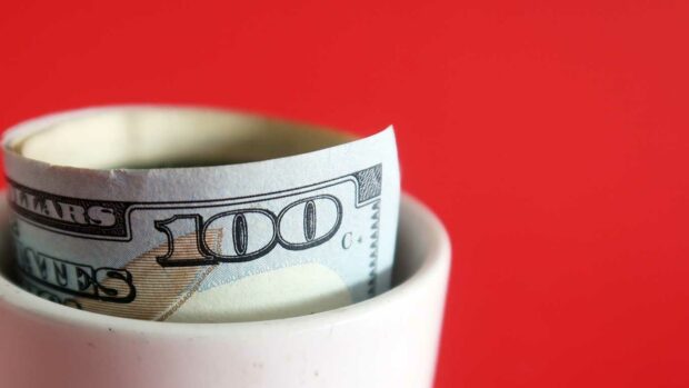 Macro of cash dollars money banknote in a white ceramic cup, on red background.