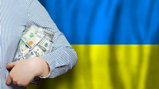 American dollars cash money in hand on flag of Ukraine