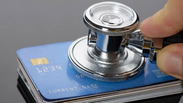 Close-up Of A Hand Holding Medical Stethoscope On Credit Card Stack