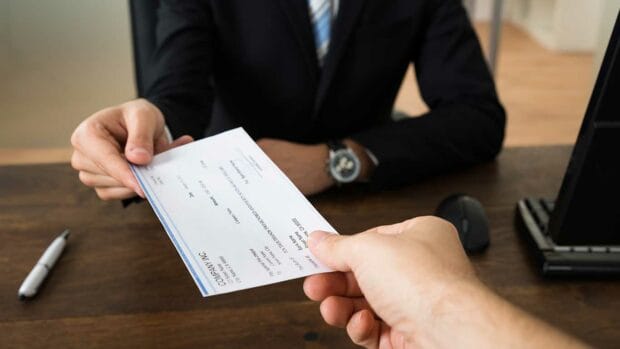 Close-up Of Businessman Hands Giving Cheque To Other Person In Office