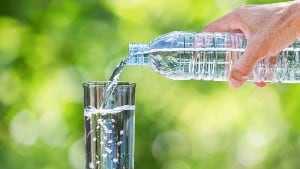 Man's hand holding drinking water bottle and pouring water into glass on wooden table