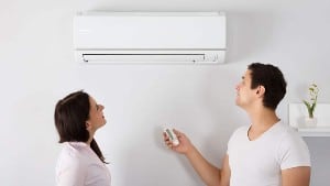Happy Young Couple Adjusting Temperature Of Air Conditioner By Remote