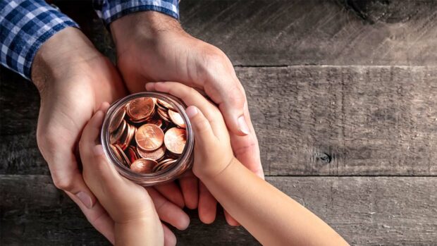 Hands Of Father Giving Jar Of Coins To Child