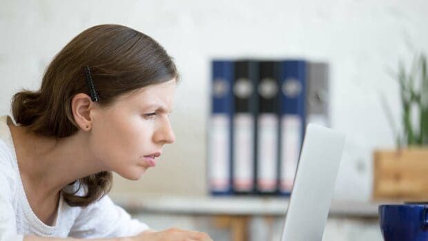 Young stressed businesswoman sitting with laptop and looking at screen with concerned facial expression.