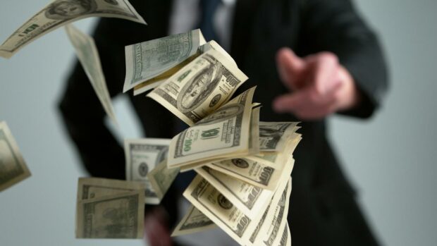 Close-up of a young businessman throwing out money banknotes isolated over gray background